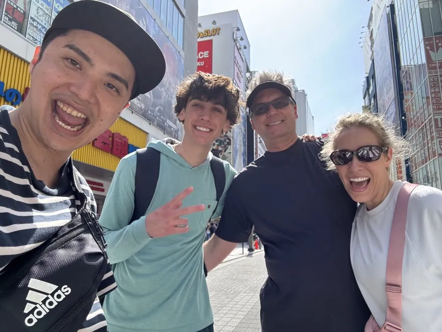 Yuuki taking a selfie with a family of guests on a sunny Akihabara street