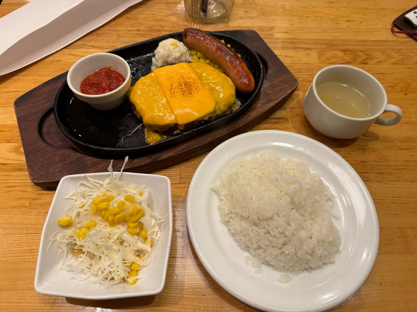 A finished cheese hamburg set: sausage, mashed potato, corn, salsa, rice and soup on the side